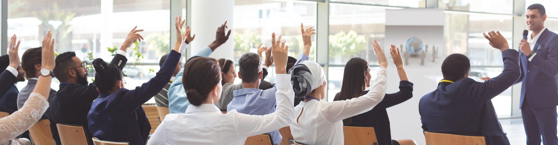 Rear view of group of diverse business people raising hands while listening to handsome biracial businessman at conference, unaltered